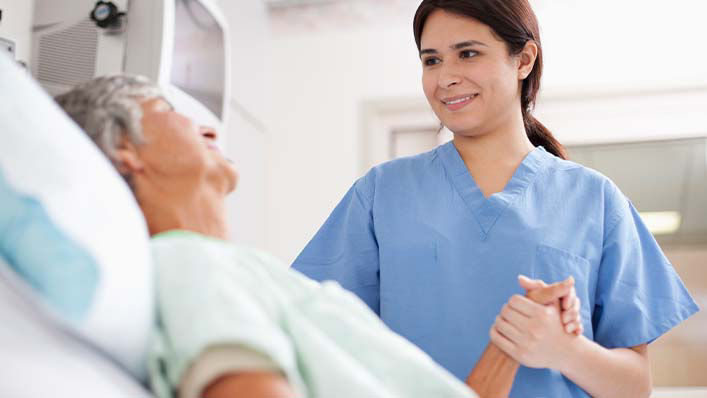 A nurse smiles and holds an older patient’s hand