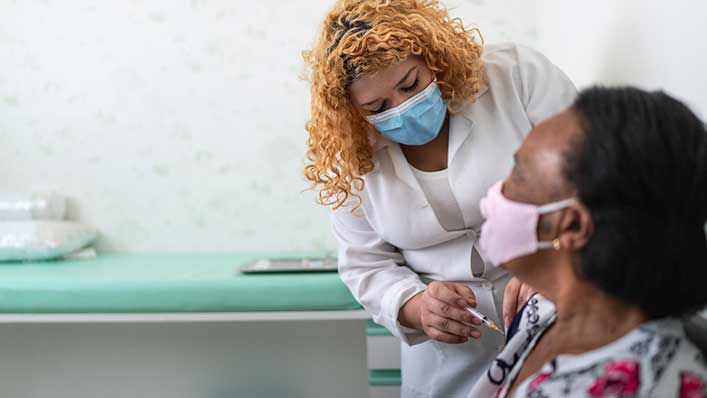 Nurse applying vaccine on patient's arm using face mask