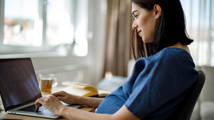 A pregnant woman uses her laptop at home.