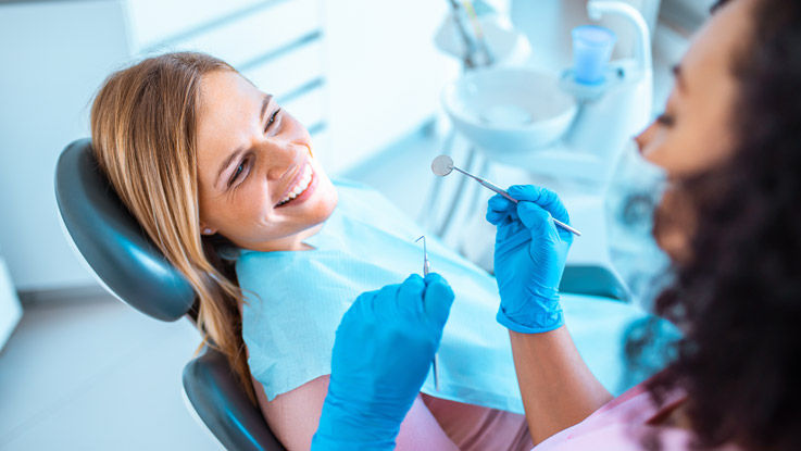 Woman smiling and sitting in a dentist's chair as the dental hygienist holds dental tools over her.