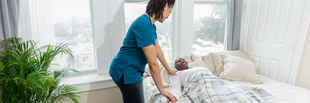 A nurse puts her hand on the shoulder of a smiling woman in a bed.