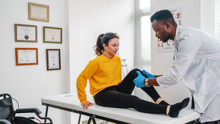 A doctor examining a young woman’s knee.