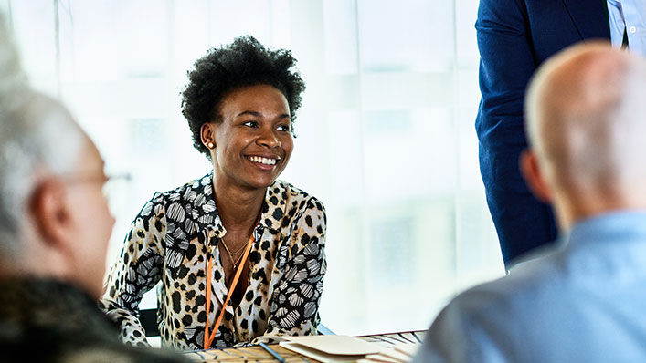 In a conference room, a young woman smiles as she meets with her coworkers.