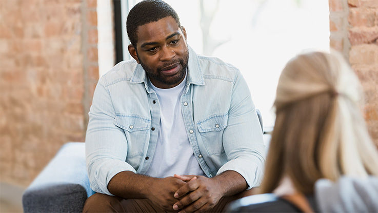 A man listens to a woman speak with a thoughtful expression on his face.