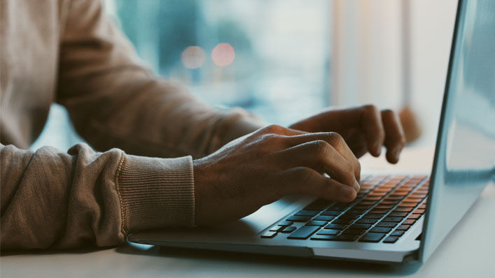 A close-up of a person typing on their laptop