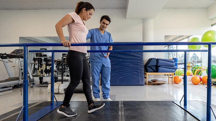 A woman with a spinal cord injury uses parallel bars while her physical therapist looks on.