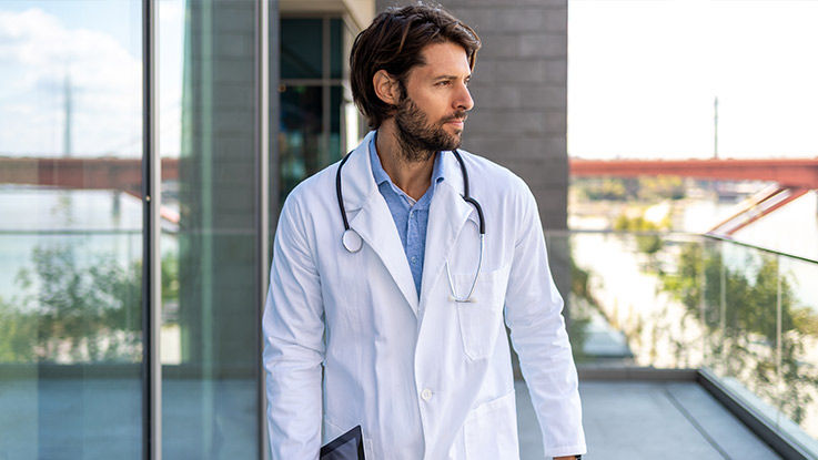 A doctor takes a break outside a health care clinic on a sunny day while looking at something in the distance