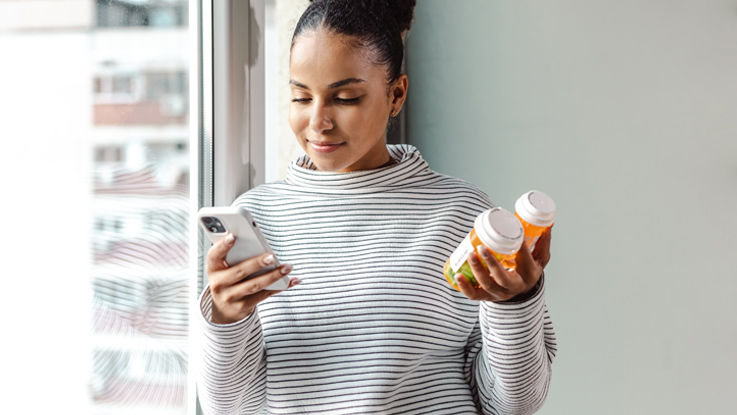 Woman holding two pill bottles looking at her phone.