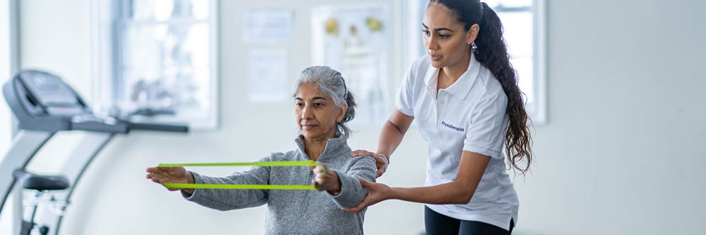 A physical therapist guides a patient through an arm exercise using a resistance band.