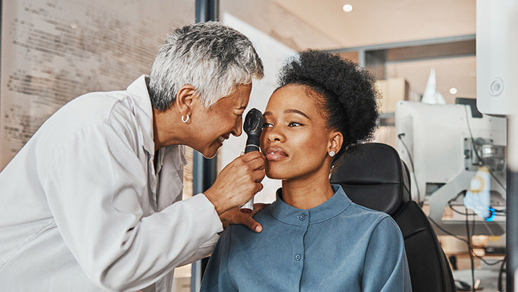 A doctor uses a handheld device to examine a woman's right eye.