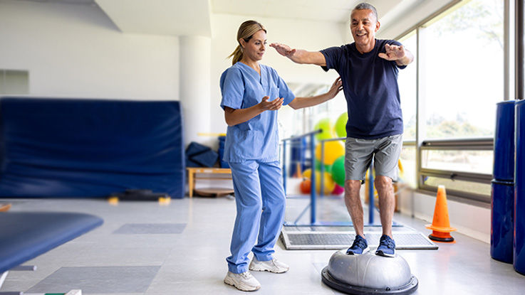 A physical therapist guides her patient through a balance exercise.