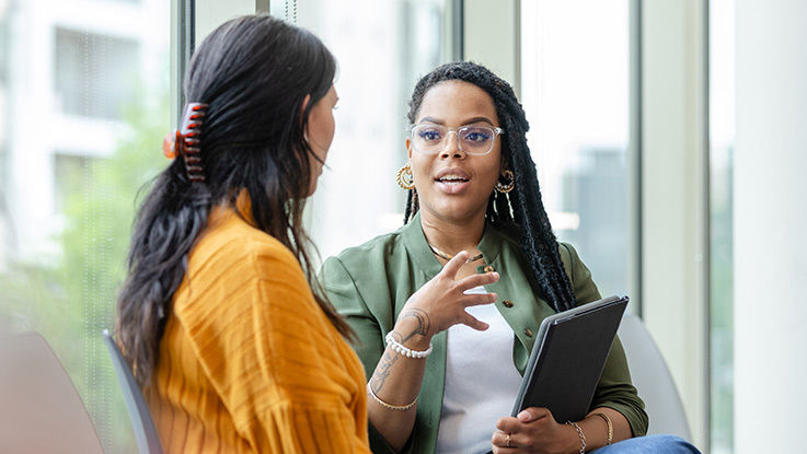 An eating disorder therapist talks with a young woman in a sunny room.