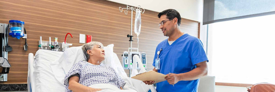 A doctor speaks with an older patient resting in a hospital bed before surgery