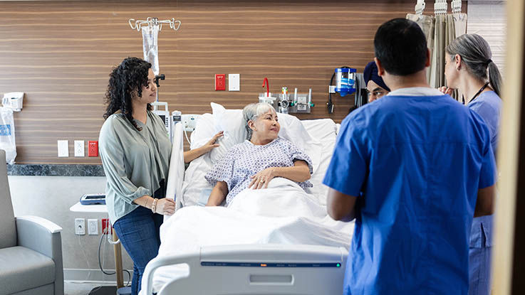 An elderly transitional care patient with her adult daughter standing by her speaks with her care team.