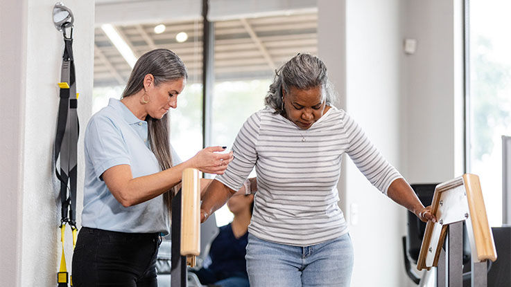A therapist helping a woman walk up some stairs in a therapy gym.