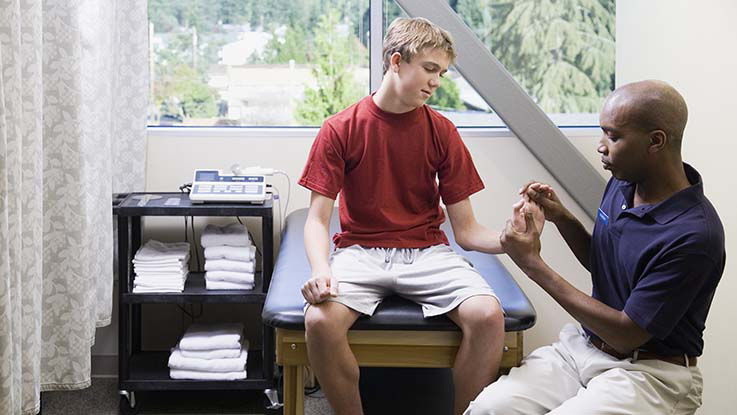 A physical therapist guides his patient through hand-strengthening exercises.