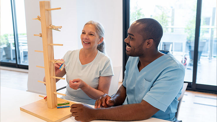 An occupational therapist guides his patient through an exercise that uses clothespins and wood pegs.