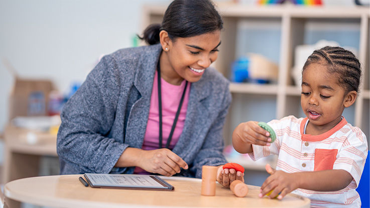 A therapist and child play with blocks and Play-Doh.