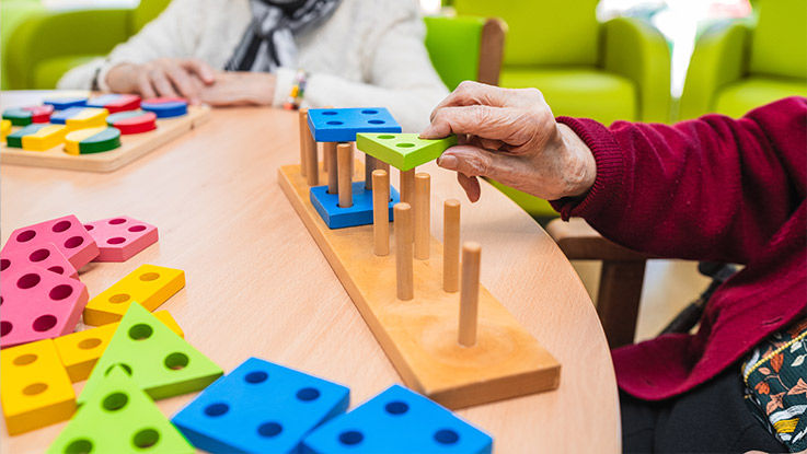 A close-up image of an older patient's hands as they play a game with wood blocks and pegs. 