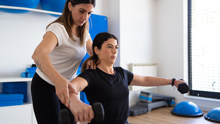 A physical therapist instructs a young woman on how to use dumbbells.