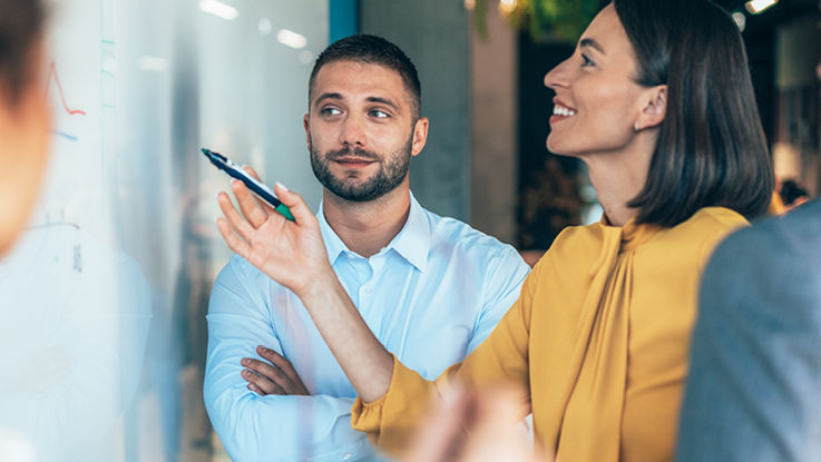 A group of colleagues converse with one another while gathered around a whiteboard