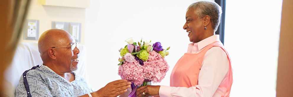 An older woman volunteer hands an older man patient a bouquet of flowers
