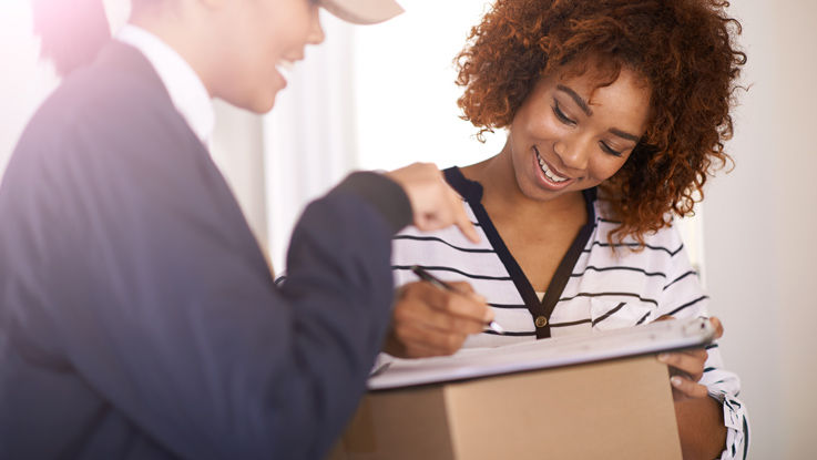 A smiling young woman signs for a package delivered by her letter carrier.
