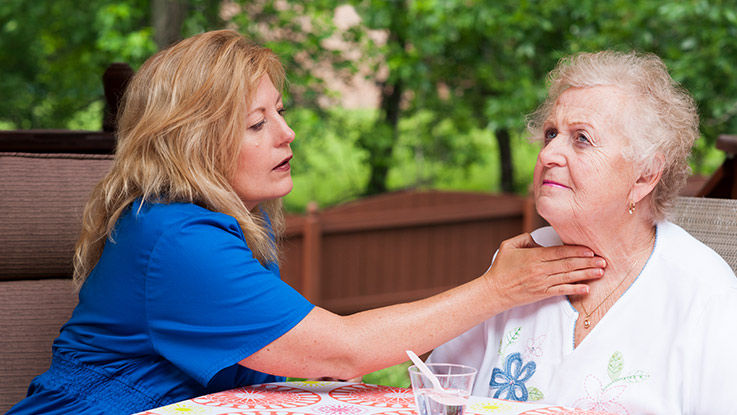 A speech therapist places a hand on her elderly patient's throat to help her swallow.