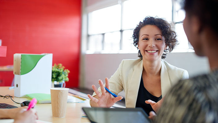 In a conference room, a woman leads a meeting at a conference table.