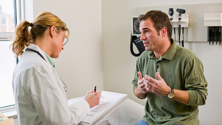 Female doctor listens as man describes his symptoms. 