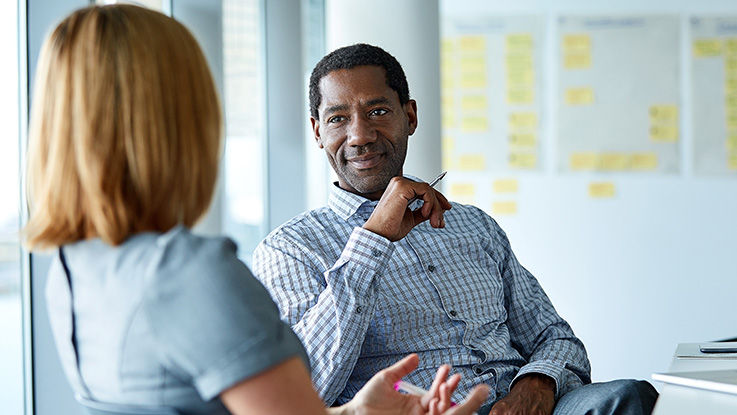 A man and a woman talk in a conference room in front of a whiteboard with notes.