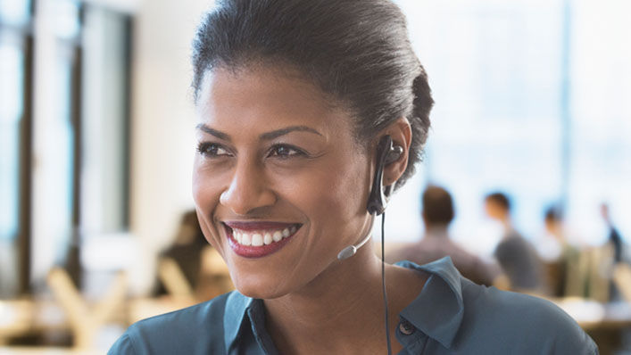 A woman wearing an earpiece smiles as she speaks with someone on the phone