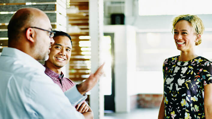 A man wearing business attire speaks to two smiling colleagues