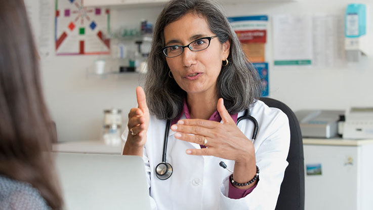 A doctor sits in her office and talks with a patient.