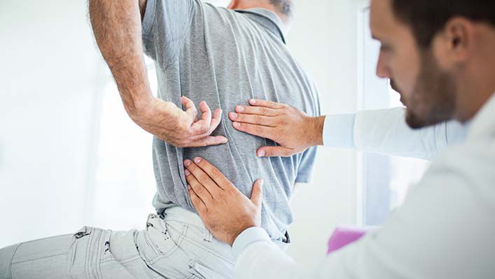 A physical therapist examines a patient's back.