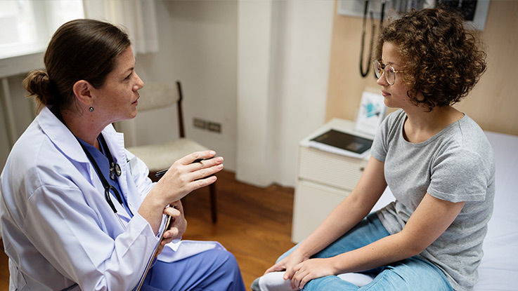 A teen girl and her female doctor talk in an exam room