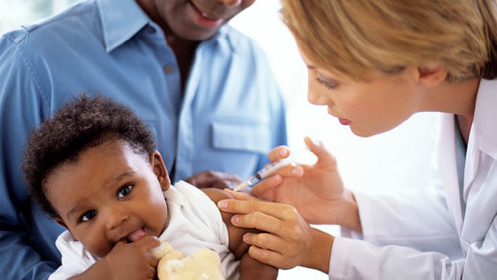 A father holds his baby while a nurse administers a shot.