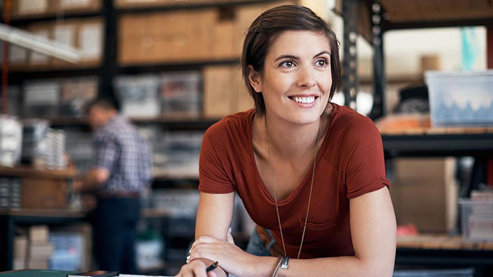 Working at a warehouse drafting table, a young woman smiles to the distance.