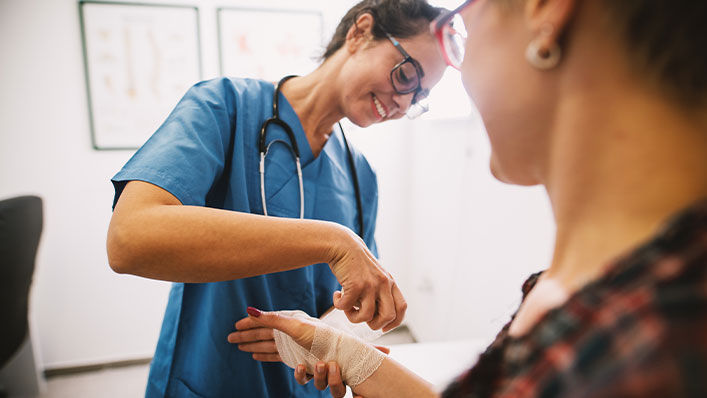 Smiling nurse wraps a woman's hand in gauze.