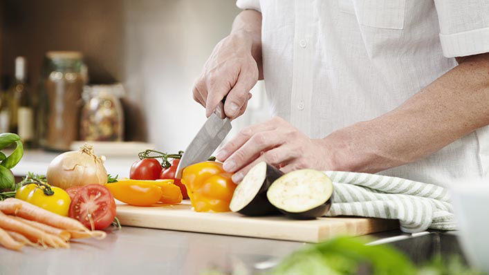 Man cutting assorted vegetables on a cutting board.