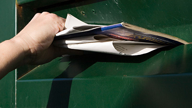 Close-up of a hand pushing papers into the slot of a recycling bin.