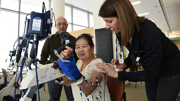 Two occupational therapists helping a woman use a machine that manipulates her hand. 