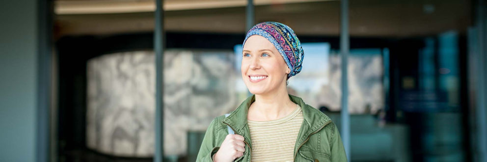 A smiling woman wearing a scarf on her head leaves the hospital.