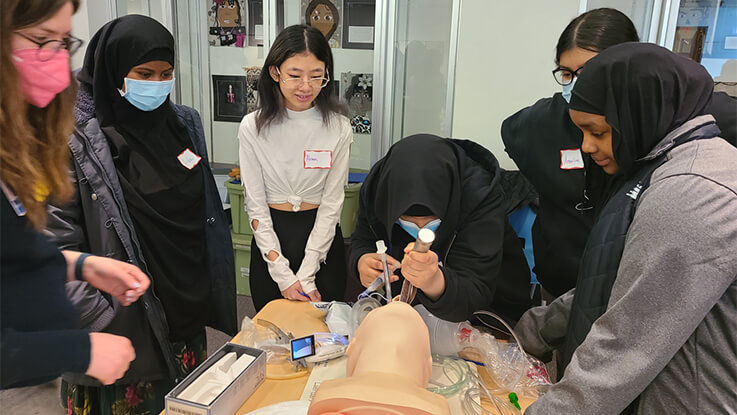 An experienced health care professional demonstrates the intubation process on a dummy for several students.