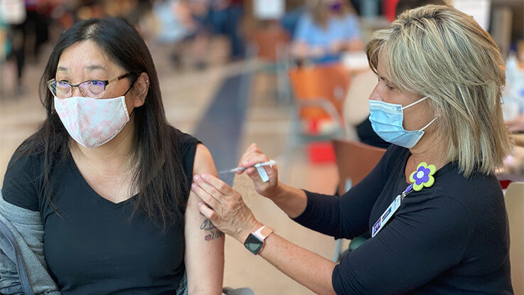 A woman receives a vaccine shot in her arm from a nurse practitioner.