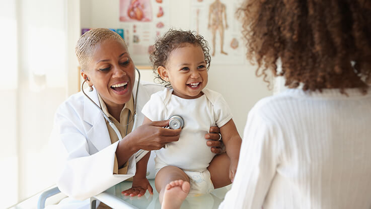 A pediatrician uses her stethoscope to listen to a baby's heart at a well-child checkup.