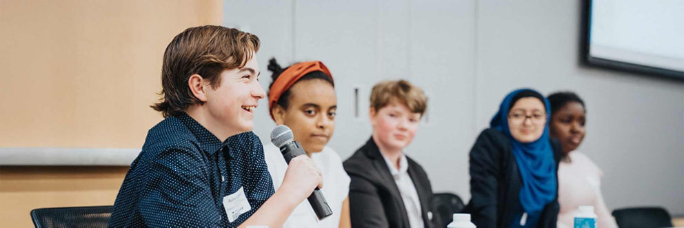 A panel of diverse teenagers speaks to an audience.