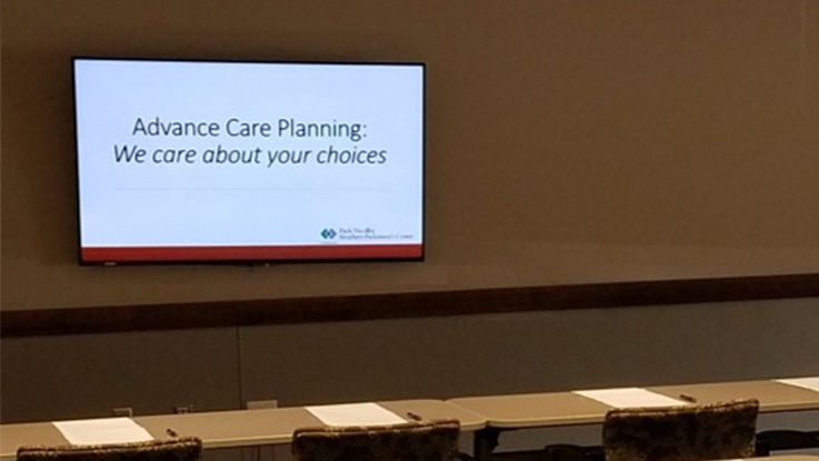 An empty classroom with "Advance Care Planning: We care about your choices" projected on the wall awaits class members.