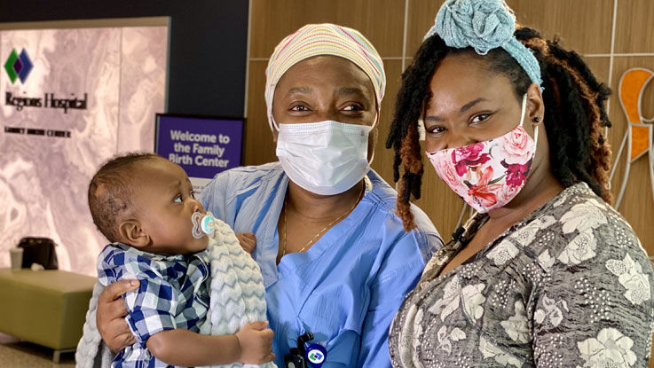 Photo of an OB-GYN at Regions Hospital holding a baby and standing next to the baby’s mom.