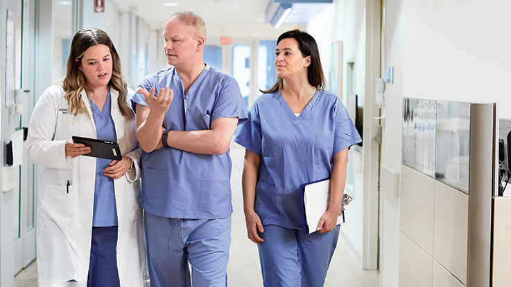 A care team walks down a hospital hallway discussing their patient’s chart.